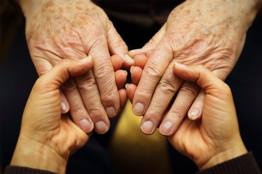 Close up of senior person's hands holding a younger person's.
