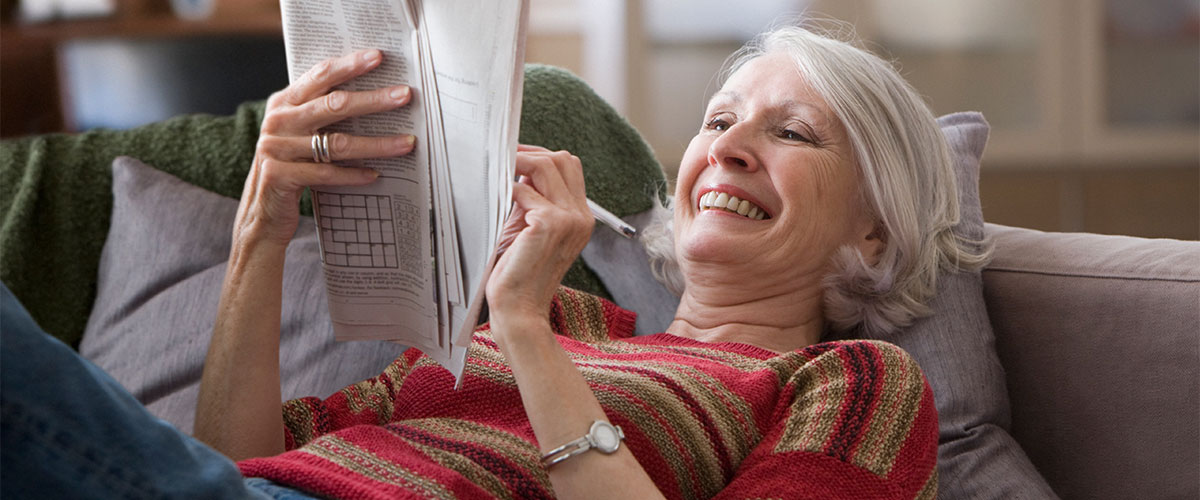 Senior woman doing a crossword on a couch