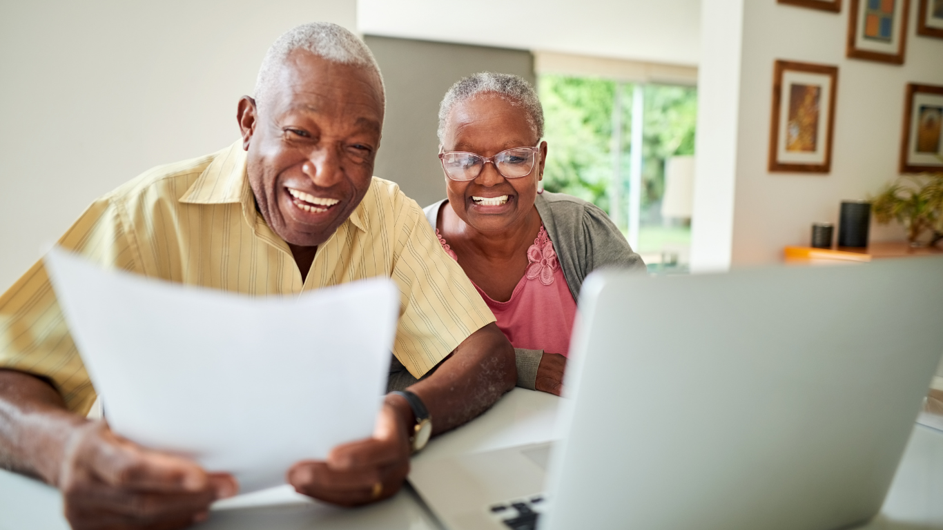 Smiling senior couple looking at computer and paperwork