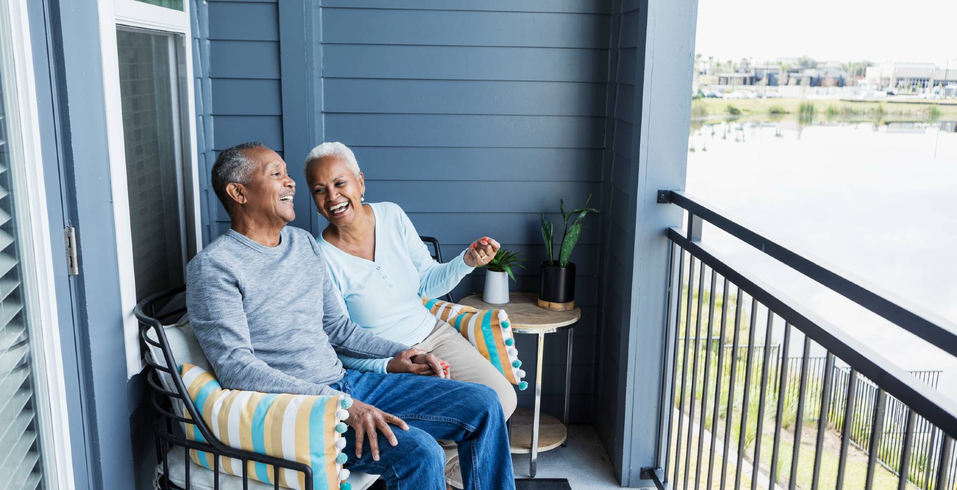 happy senior couple enjoying their balcony at their senior condo overlooking a lake