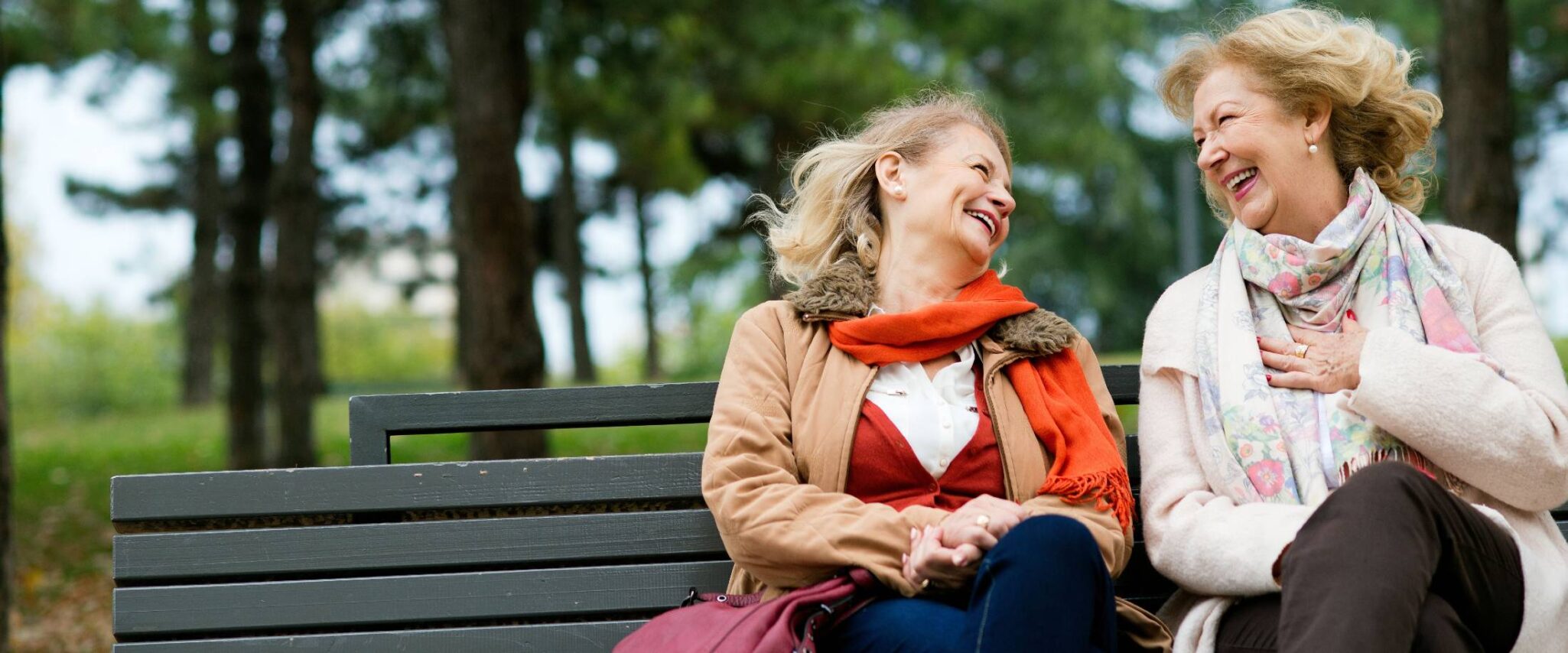 two senior living residents sitting on a bench laughing