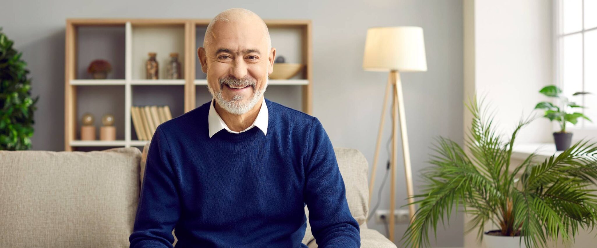 happy senior man sitting on the couch inside his senior apartment