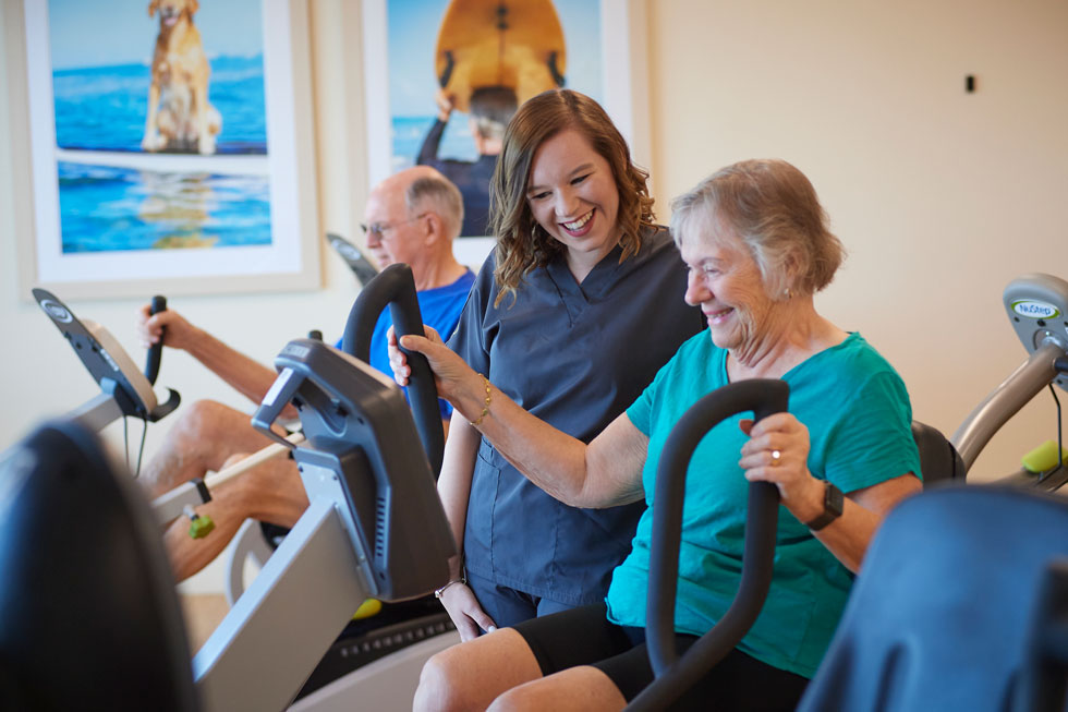 A senior man and woman exercise on stationary bikes.