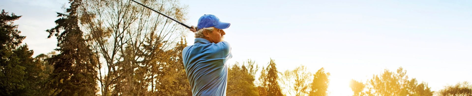 A senior man mid golf swing 