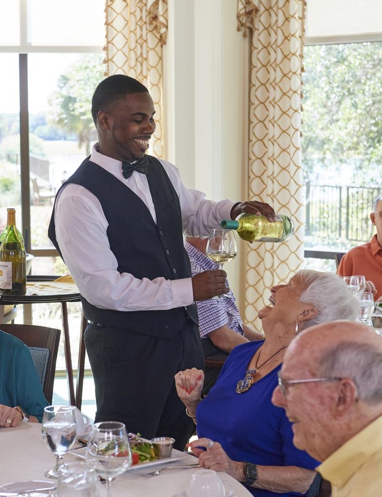 A server pouring a glass of wine for a resident.