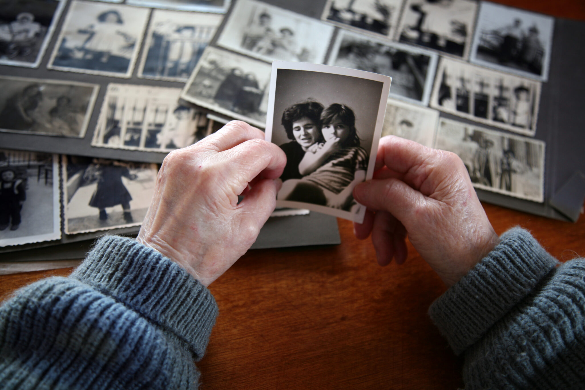 Focus on the hands of an elderly person holding black and white photos while looking at a photo album