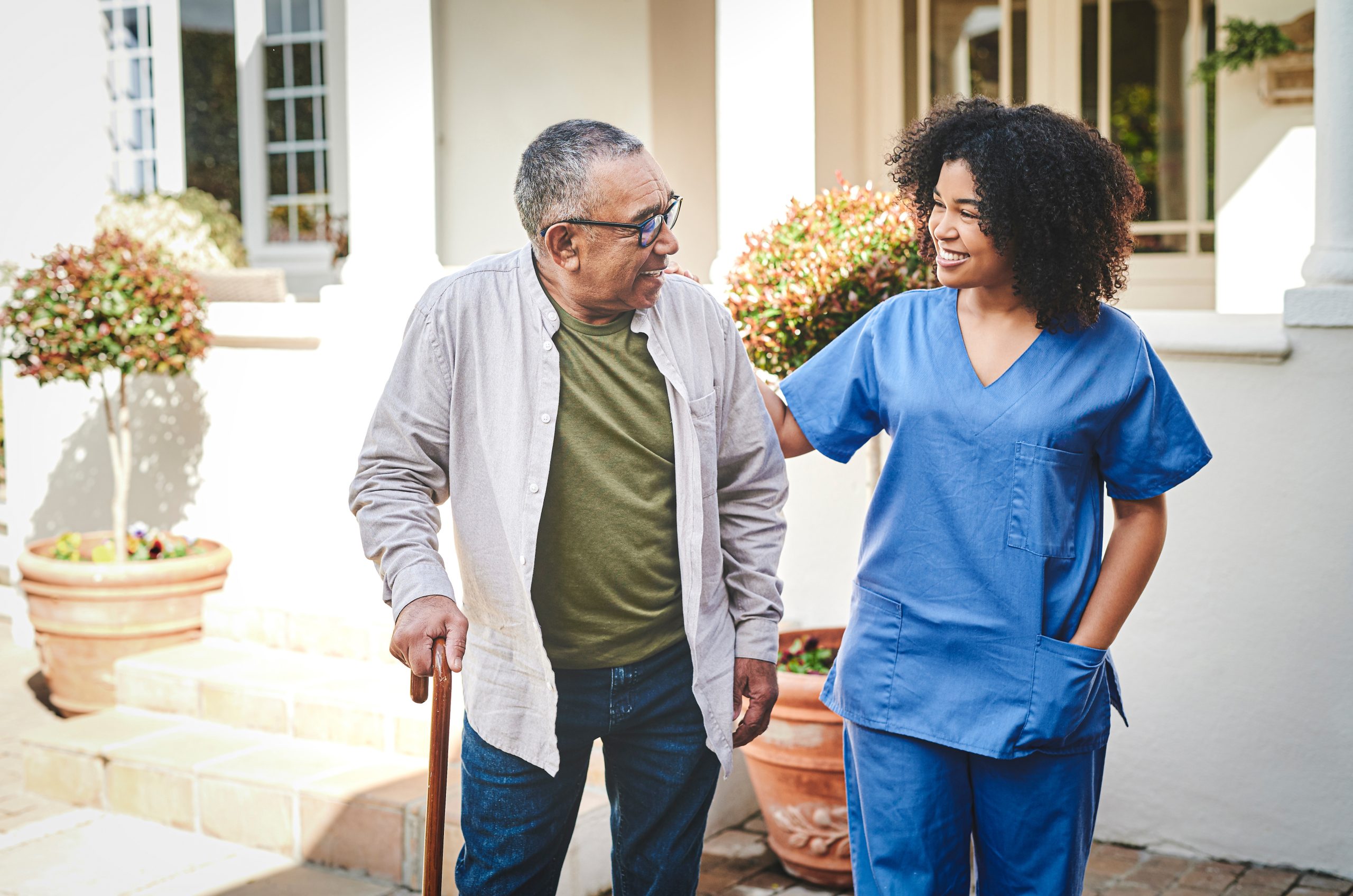 Female healthcare worker on outdoor walk with senior man with cane