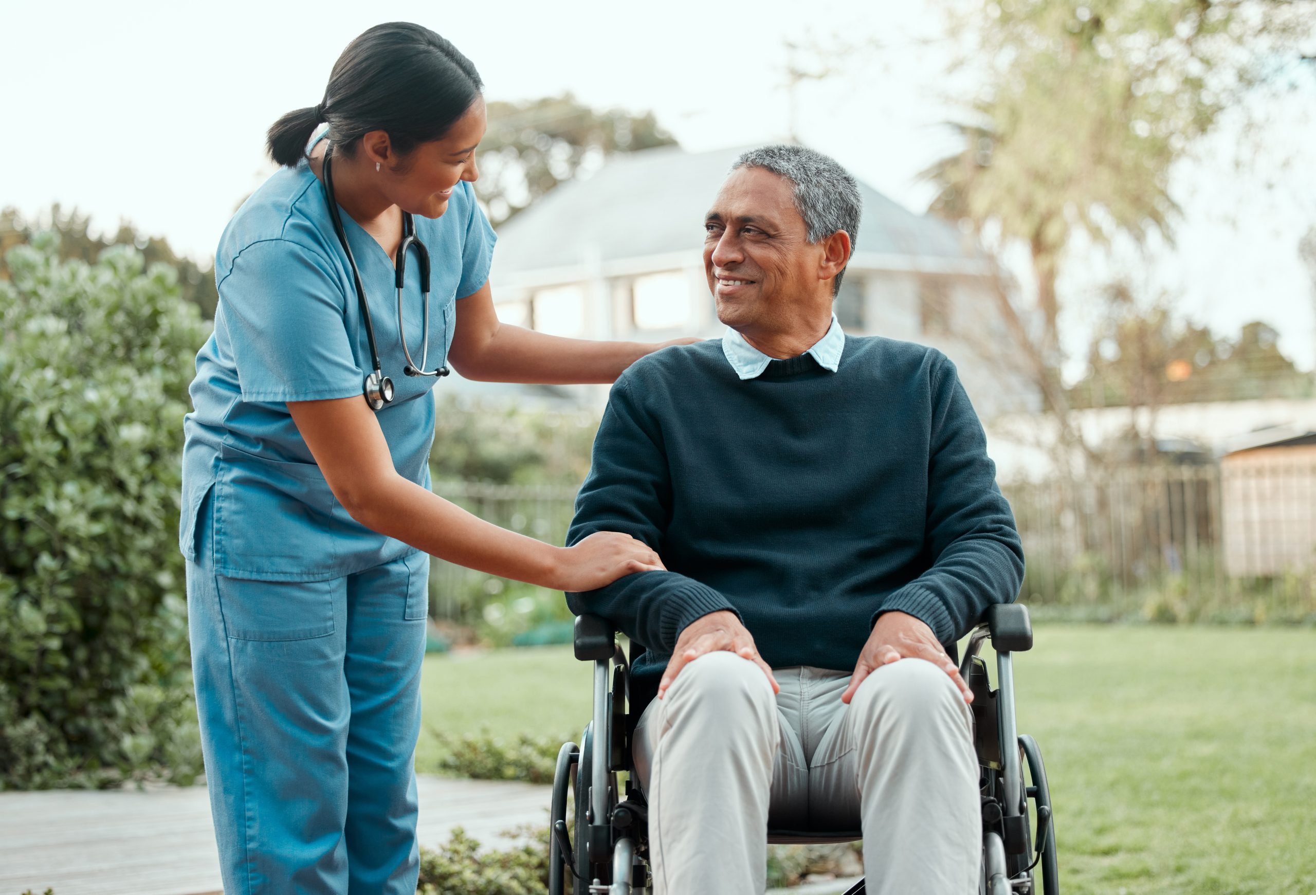 Female healthcare worker assisting senior man in wheelchair while outdoors