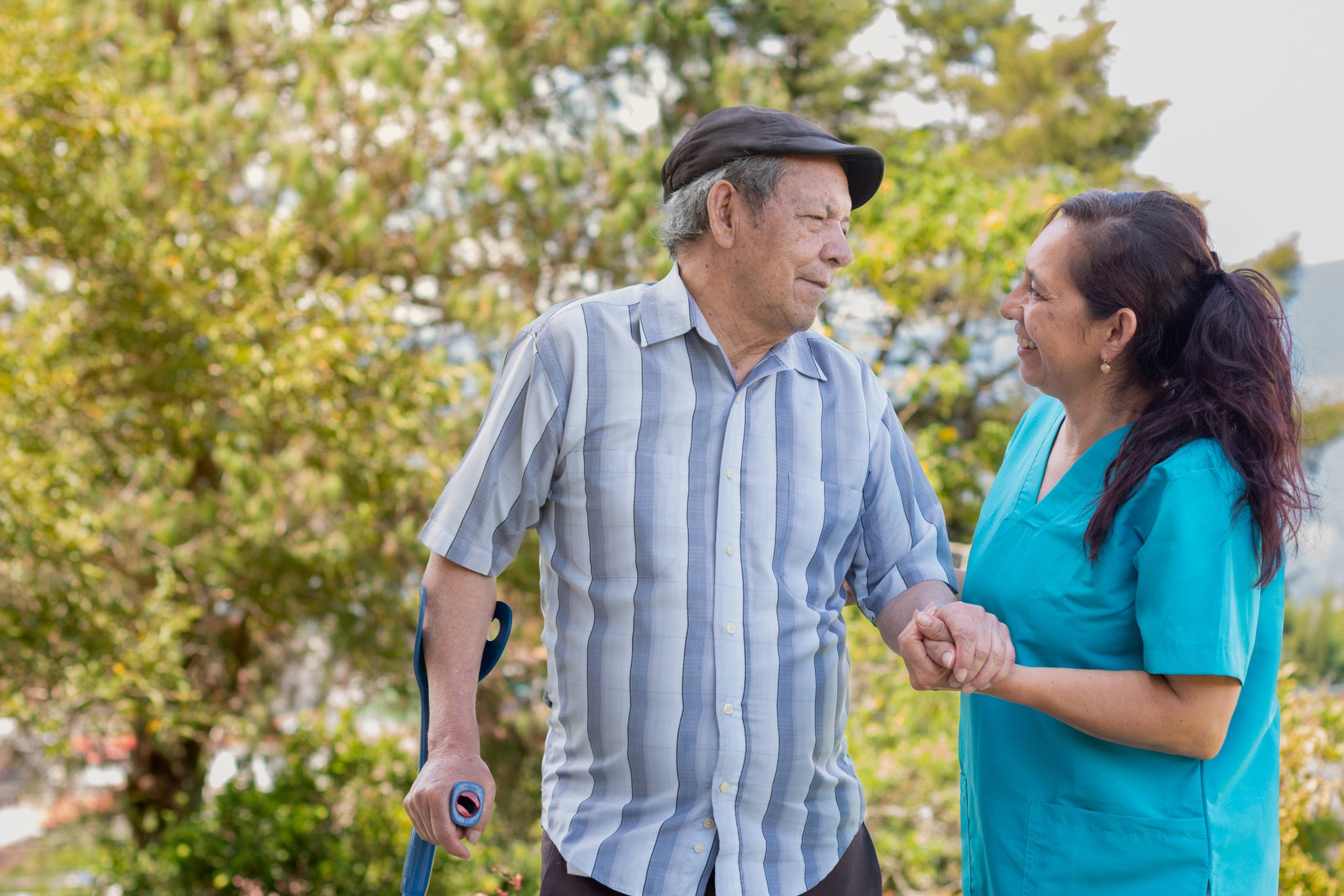 Female healthcare worker assisting senior man with cane on outdoor walk