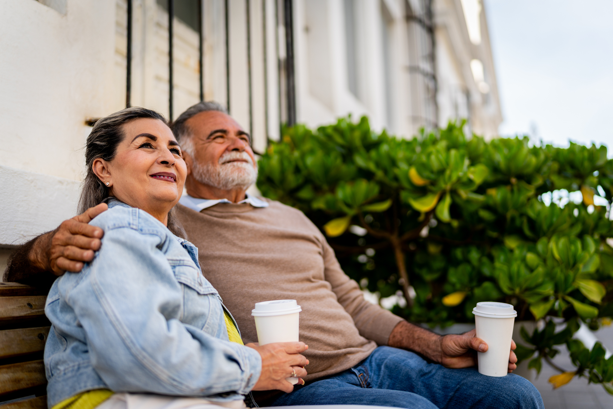 Senior couple sitting outside while holding cups of coffee
