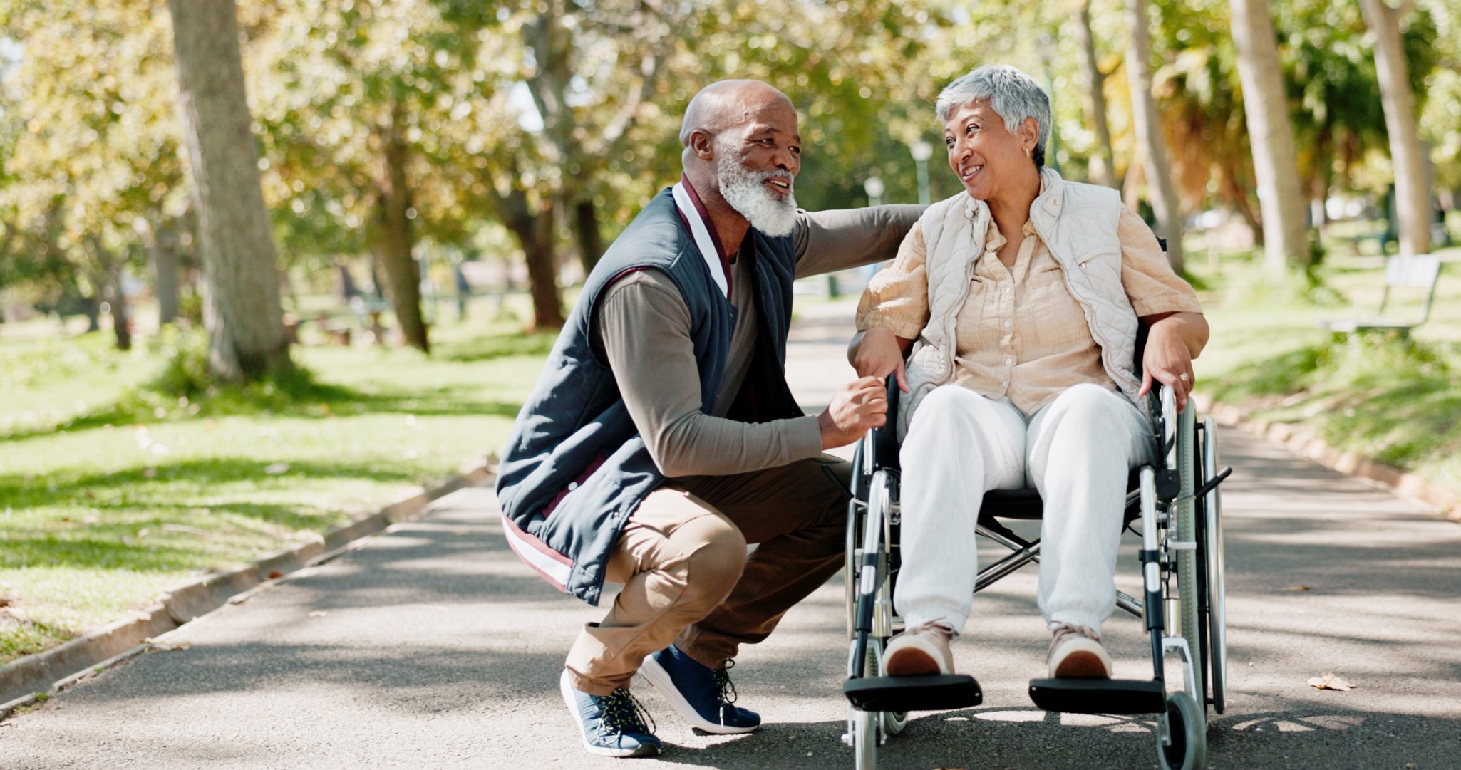 Senior woman in wheelchair on outdoor walk with senior man